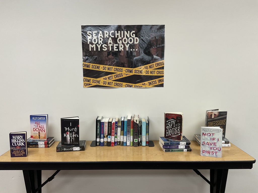 Books displayed on table with mystery genre sign
